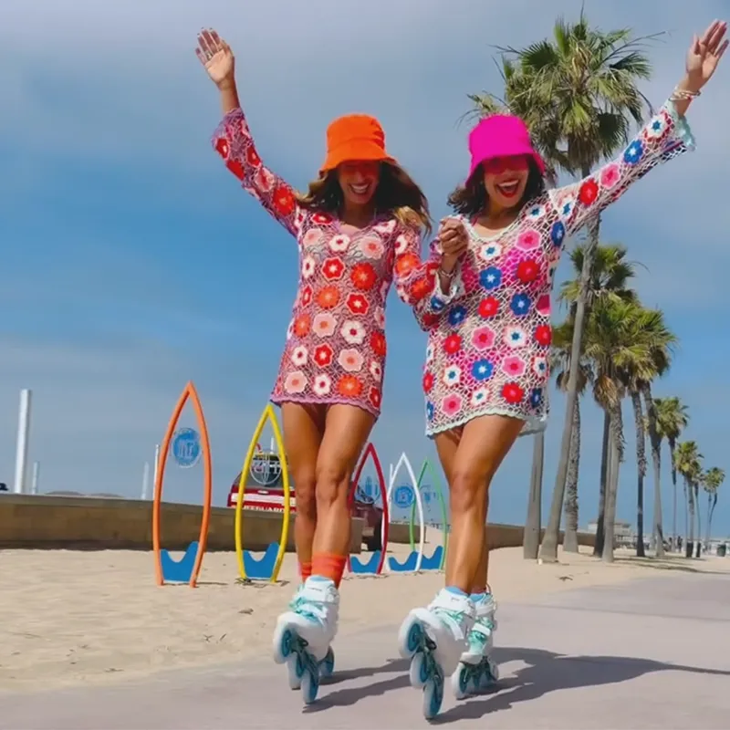 Two women in colorful floral dresses and hats rollerblading on a beach.