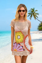 Woman wearing a colorful crochet dress on a beach with palm trees in the background