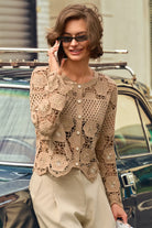 A woman wearing a beige crochet cardigan with pearl buttons and cream trousers, standing outdoors next to a vintage car and talking on a phone.