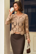 A woman wearing a beige crochet cardigan with button details and a dark brown pencil skirt, holding a white mug and a small brown handbag.