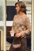 A woman wearing a beige crochet lace cardigan with button details, paired with a dark brown skirt and carrying a brown crocodile-embossed shoulder bag, standing in front of a glass storefront.
