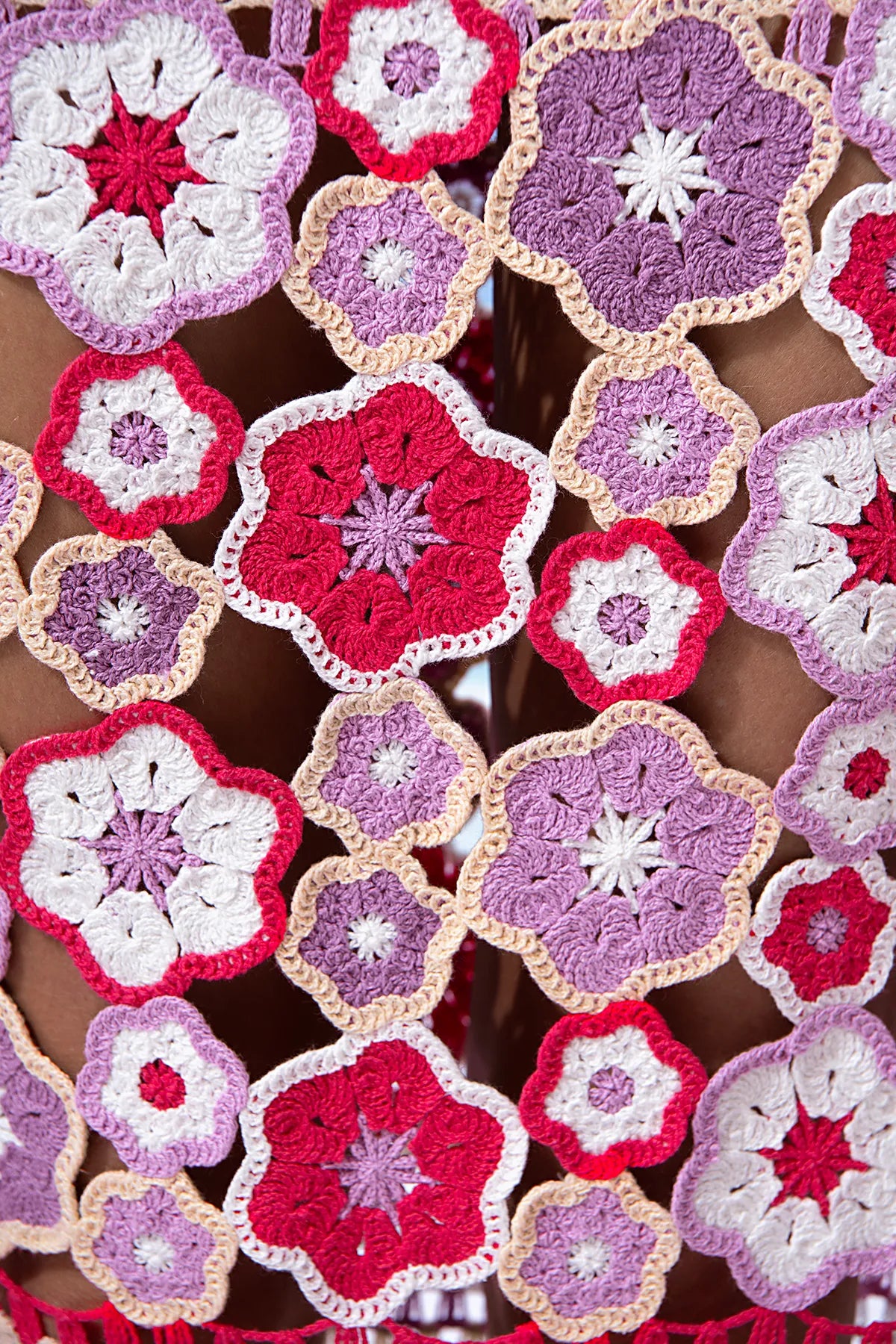 Close-up of crocheted flower patterns in red, pink, and purple on a textured surface.