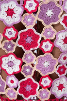 Close-up of crocheted flower patterns in red, pink, and purple on a textured surface.