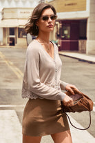A woman wearing a light beige button-front cardigan with lace trim and a brown mini skirt, holding a brown leather handbag on a city street.