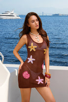 Woman wearing a brown crochet dress with starfish patterns on a boat with a yacht in the background.