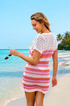 Woman wearing a colorful striped dress on a beach with clear blue water and sky.