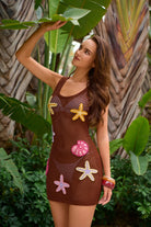 Woman wearing a brown mesh dress with starfish and shell designs in a tropical setting.