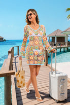 Woman in a floral dress standing on a wooden pier by a pool, holding a suitcase and a polka dot bag.