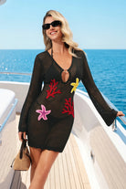 Woman in a black crochet dress with colorful starfish patterns on a boat deck.