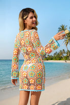 Woman in a colorful floral dress on a beach with palm trees in the background