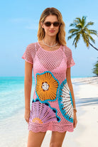Woman wearing a pink crochet dress with floral patterns on a beach.