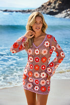 Woman wearing a colorful crochet cover-up on a beach with ocean and rocks in the background