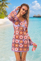 Woman in a colorful floral dress standing on a beach with palm trees and clear blue water.
