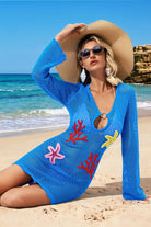 Woman in a blue beach cover-up with coral designs on a sandy beach.