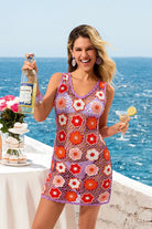 Woman in a colorful crochet dress holding a bottle and glass by the ocean.